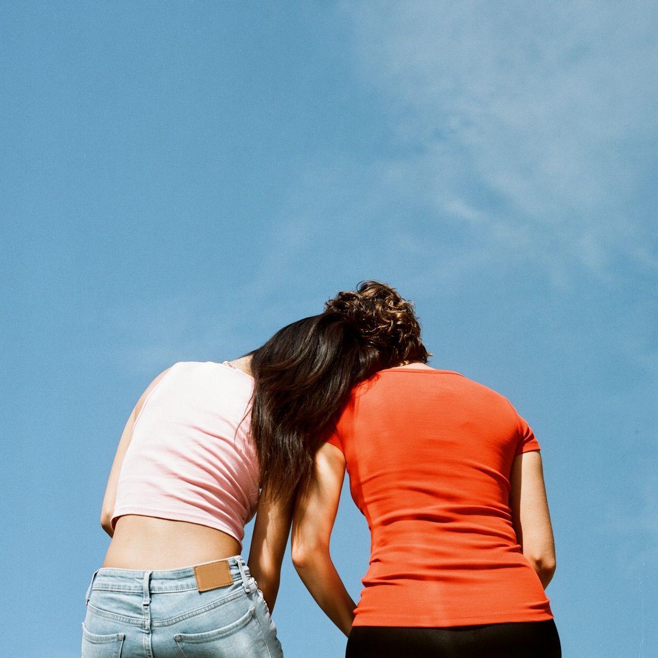 Two students leaning together under a blue sky